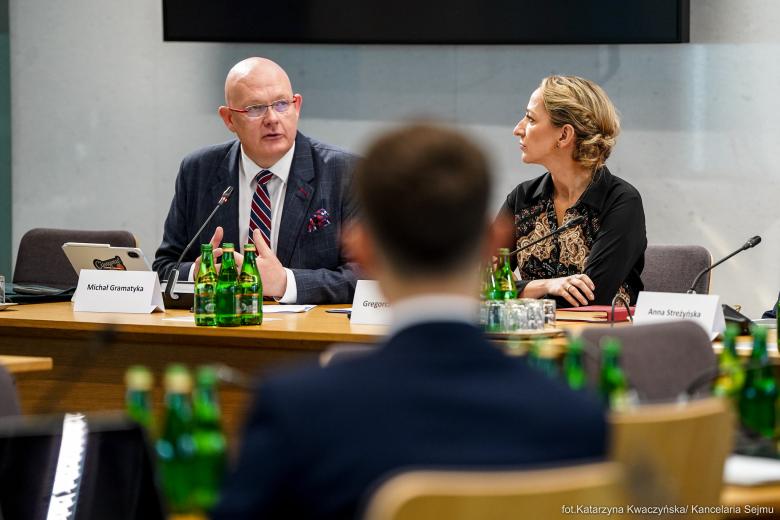 Dwie osoby siedzą za stołem w sali konferencyjnej
