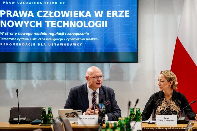 Dwie osoby siedzą za stołem w sali konferencyjnej