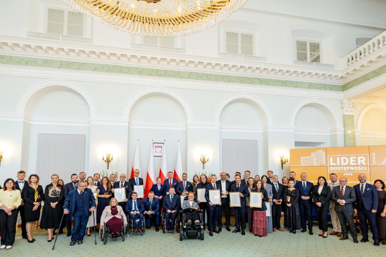 Kilkadziesiąt osób pozuje na stojąco do wspólnego zdjęcia w zabytkowym pomieszczeniu