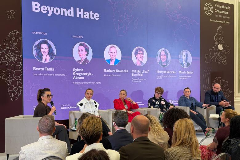 Siedem osób siedzi w fotelach na scenie podczas panelu dyskusyjnego