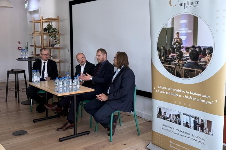 Cztery osoby siedzą przy stole na sali konferencyjnej i rozmawiają