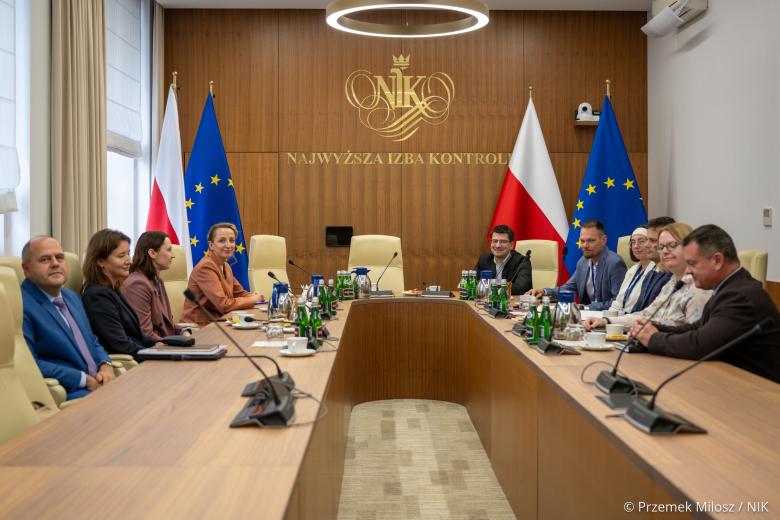 Dziesięć osób siedzi po dwóch stronach dużego stołu w sali konferencyjnej i rozmawia, w tle na ścianie duży napis: NIK Najwyższa Izba Kontroli