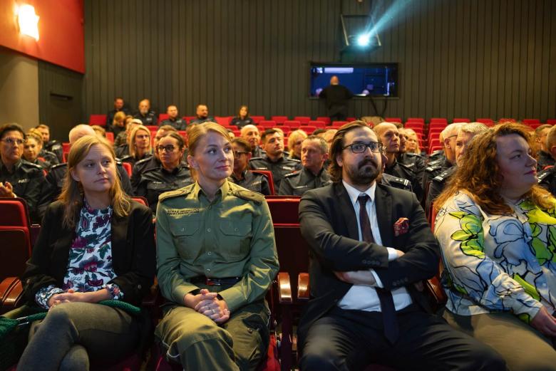Kilkadziesiąt osób siedzi w fotelach na widowni w teatrze i słucha wystąpienia