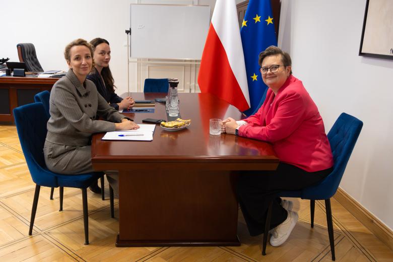 Trzy osoby siedzą przy stole w gabinecie i rozmawiają