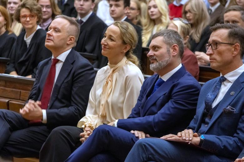Cztery osoby siedzą w pierwszym rzędzie ław na auli wykładowej, za nimi widać kilkudziesięciu słuchaczy