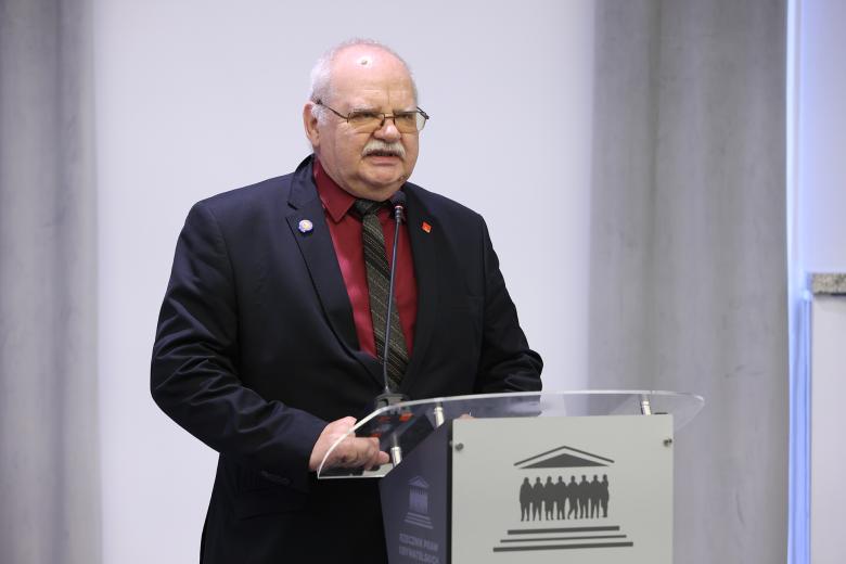 Zygmunt Wierzyński stoi przy mównicy z mikrofonem i wypowiada się