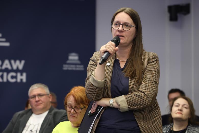 Osoba z publiczności stoi i wypowiada się do mikrofonu.