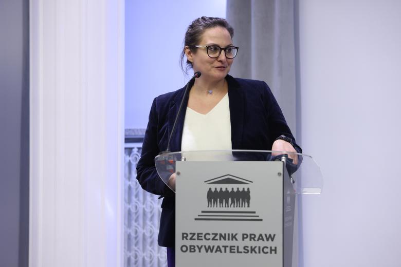 Kobieta stoi przy mównicy i wypowiada się do mikrofonu