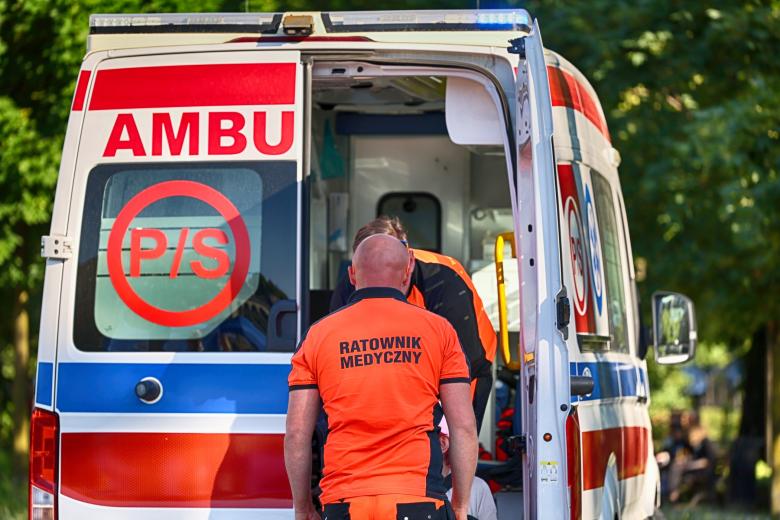 Osoba w jaskrawym uniformie z napisem "Ratownik Medyczny" stoi obok ambulansu