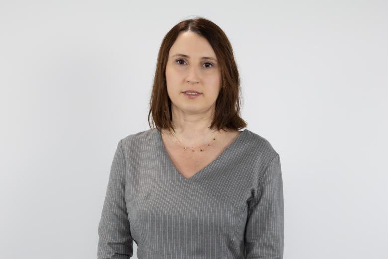 Portret Moniki Wiszyńskiej-Rakowskiej - kobieta z ciemnymi włosami w szarej bluzce na jasnym tle