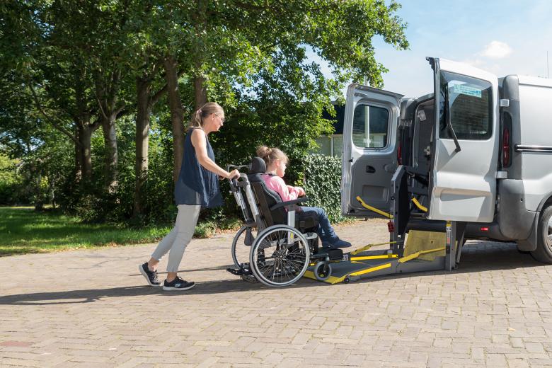 Kobieta prowadzi wózek, na którym siedzi dziewczynka, na rampę samochodu do transportu osób z niepełnosprawnościami