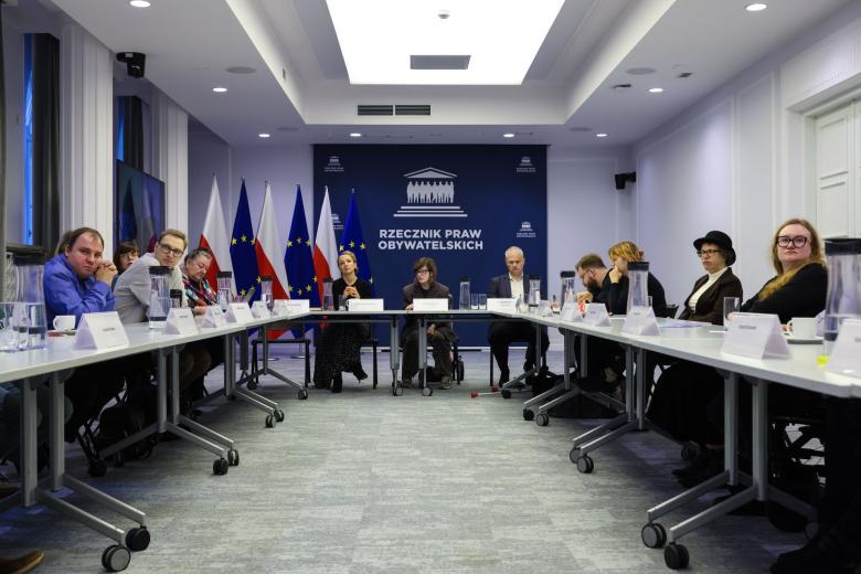 Kilkanaście osób siedzi przy stołach ustawionych w podkowę, w tle na ścianie duże logo Biura RPO