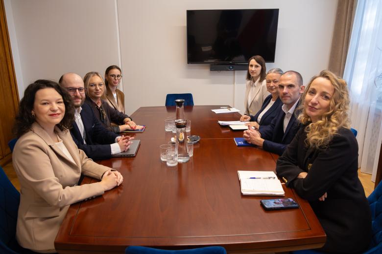 Osiem osób siedzi przy stole w salce konferencyjnej i rozmawia