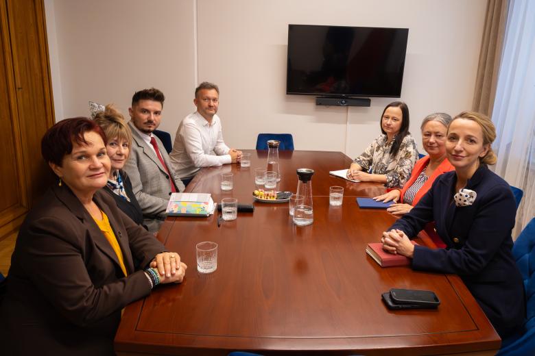 Siedem osób siedzi przy stole w salce konferencyjnej