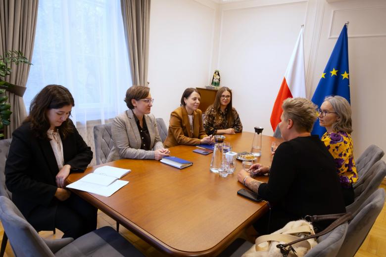 Sześć osób siedzi przy stole w sali konferencyjnej i rozmawia