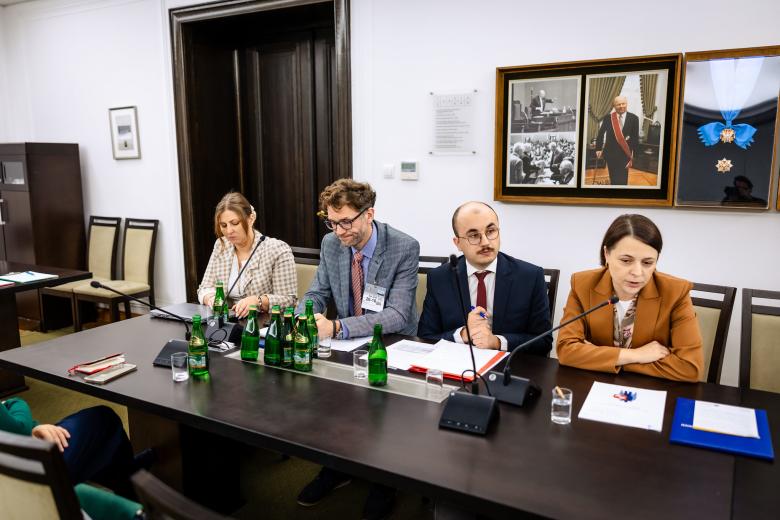 Cztery osoby siedzą za stołem, jedna z nich się wypowiada