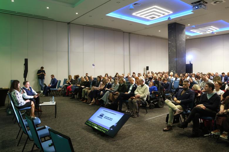 Kilkadziesiąt osób siedzi na krzesłach na dużej sali konferencyjnej