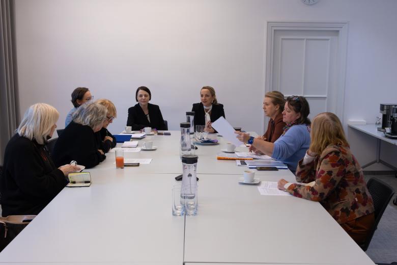 Dziewięć kobiet siedzi wokół stołu konferencyjnego i rozmawia