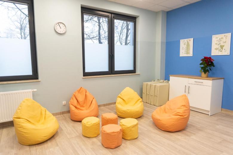 Jasny pokój z kolorowymi fotelami i pufami na podłodze, ściany pomalowane na pastelowe kolory, na ścianach wiszą obrazki