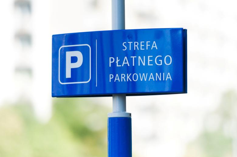 Niebieska tabliczka z dużą literą P w kwadracie i napisem "strefa płatnego parkowania" przymocowana do słupka