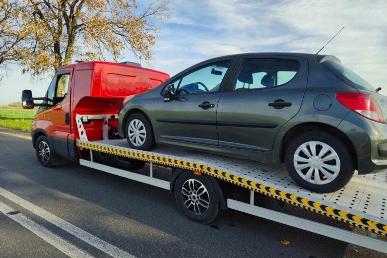 Samochód osobowy stoi na lawecie do przewożenia pojazdów na poboczu drogi