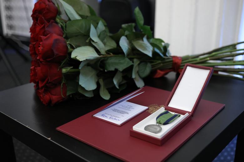 Bukiet czerwonych róż oraz dyplom i odznaka honorowa leżą na eleganckim stole