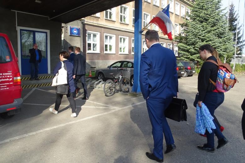 Grupa ludzi wchodzi do budynku szkoły z panstwową i unijną flagą