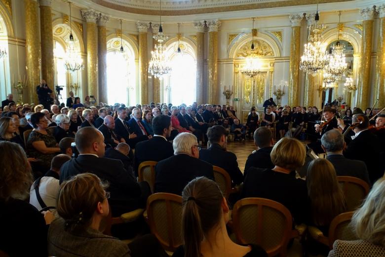 zdjęcie: kiladziesiąt osób siedzi na sali, z boku widać stojącego skrzypka