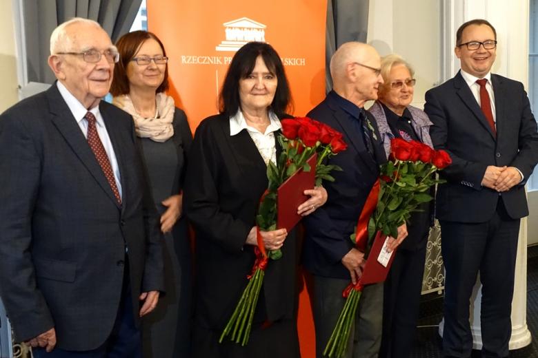 zdjęcie: trzy kobiety i trzech mężczyzn stoją obok siebie, kobieta i mężczyzna po środku trzymają bukiety czerwonych róż