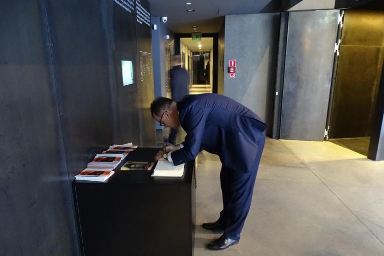 Zdjęcie: pochylony męzczyzna wpisuje się do księgi pamiątkowej w muzeum