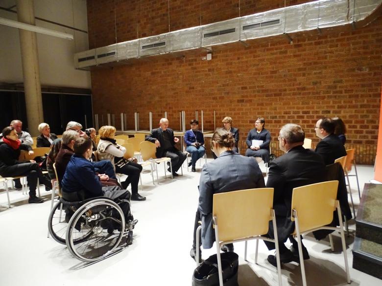 Zdjęcie: uczestnicy spotkania siedzą w kręgu. Na pierwszym planie osoba na wózku inwalidzkim
