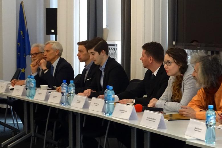 zdjęcie: przy białych stołach siedzi kilka osób, w roku sali widać flagę Unii Europejskiej