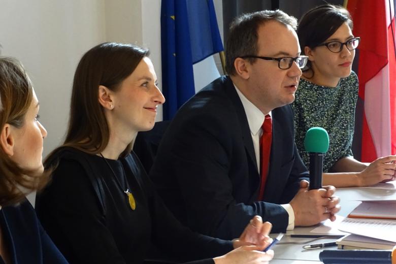 zdjęcie: z profilu widać trzy kobiety i mężczyznę w garniturze, który mówi do mikrofonu