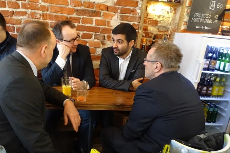 zdjęcie: przy małym stoliku w kawiarni siedzi czterech mężczyzn w garniturach