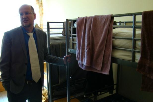 zdjęcie: mężczyzna w krawacie i garniturze stoi przy piętrowych łóżkach