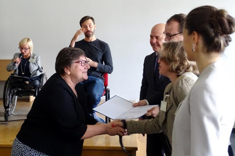 zdjęcie: kobieta odbiera dyplom od kilku osób, które stoją po prawej stronie