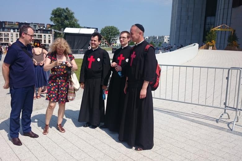 Zdjęcie: grupa ludzi w tym zakonnicy w sutannach z czerwonymi krzyżami