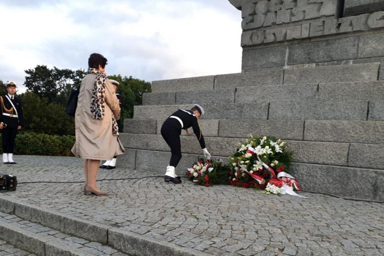 kobieta stoi, mężczyzna w mundurze składa wieniec pod pomnikiem