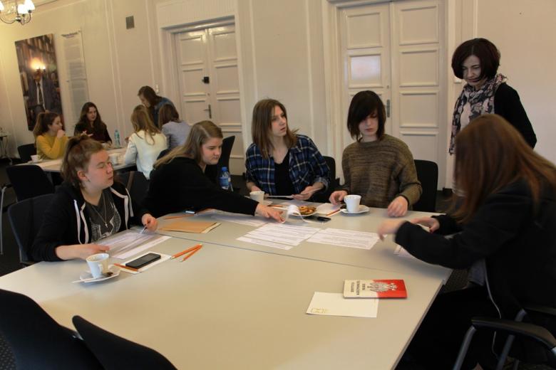 zdjęcie: pięć dziewczyn siedzi wokół kwadratowego stołu, na stole leży biało-czerwona książka z napisem Konstytucja Rzeczypospolitej Polskiej