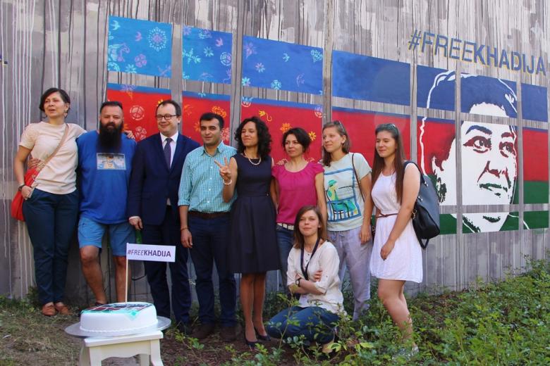 zdjęcie: grupa osób stoi na tle muralu, przed nimi na białym stoliczku stoi tort