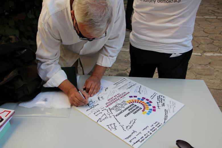 Mężczyzna w białej koszuli podpisuje plakat z podziękowaniami dla RPO