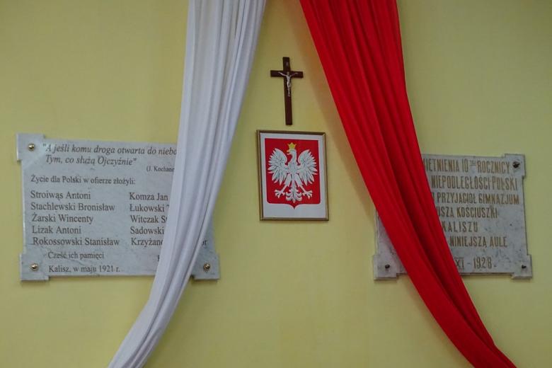 Dwie tablice na ścianie, biało-czerwona flaga i krzyż