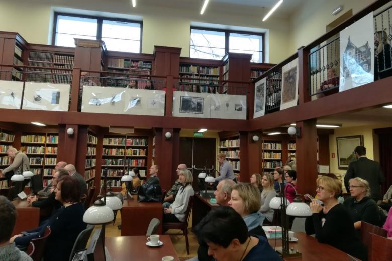 Widok na salę biblioteczną i antresole, na której siedzą ludzie młodzi