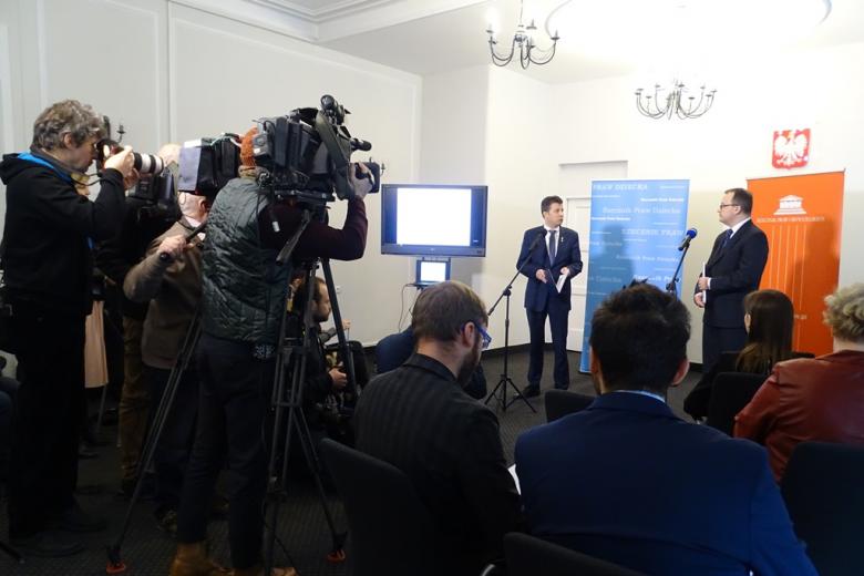 Konferencja prasowa - dziennikarze, kamery i dwaj męzczyźni na tle bannerów RPD (niebieskiego) i RPO (pomarańczowego)
