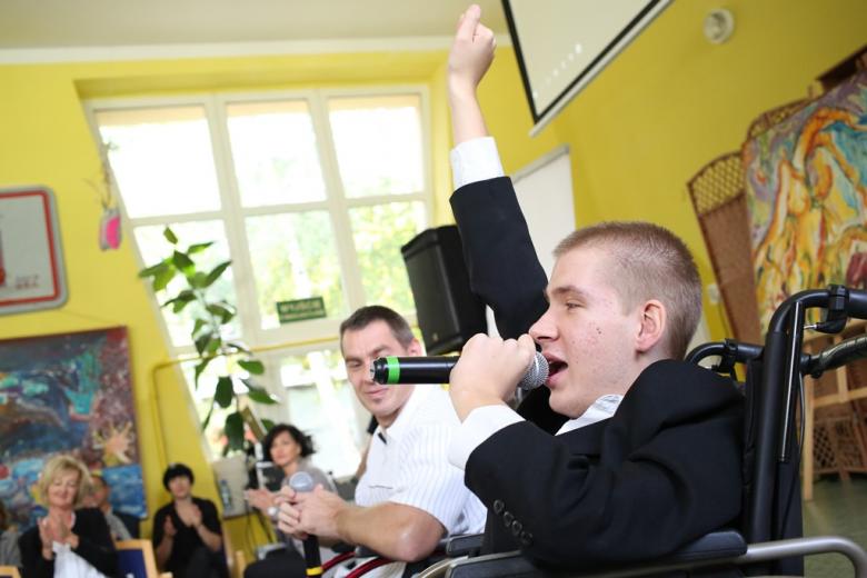 Młody mężczyzna na wózku śpiewa i podnosi rękę