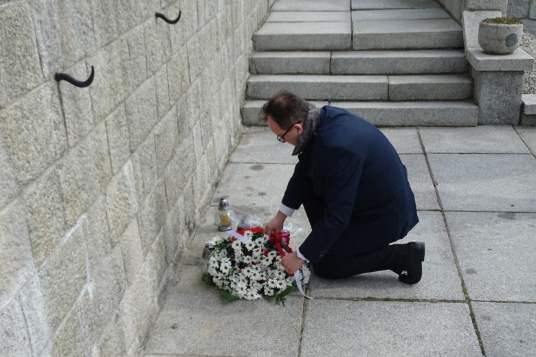 Mężczyzna klęcząc kładzie biało-czerwone kwiaty pod pomnikiem