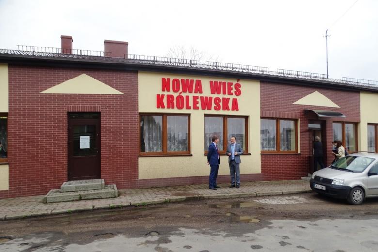 Dwaj mężczyźni przed budynkiem z napisem Nowa Wieś Królewska