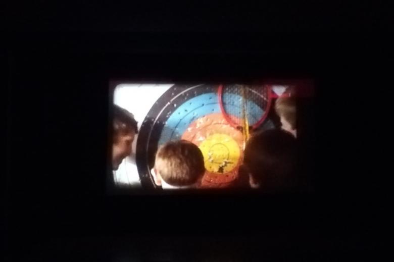 Kadr z filmu na ciemnym tle: dzieci patrzą na tarczę łuczniczą