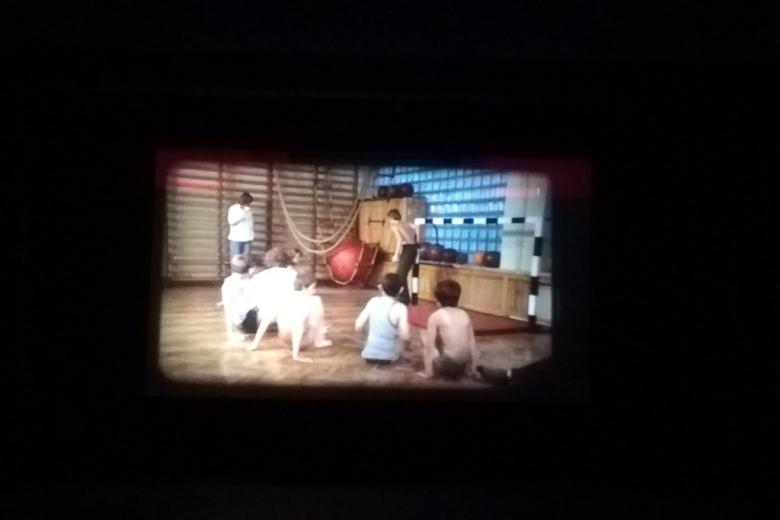 Kadr z filmu na ciemnym tle: dzieci ćwiczą na sali gimnastycznej