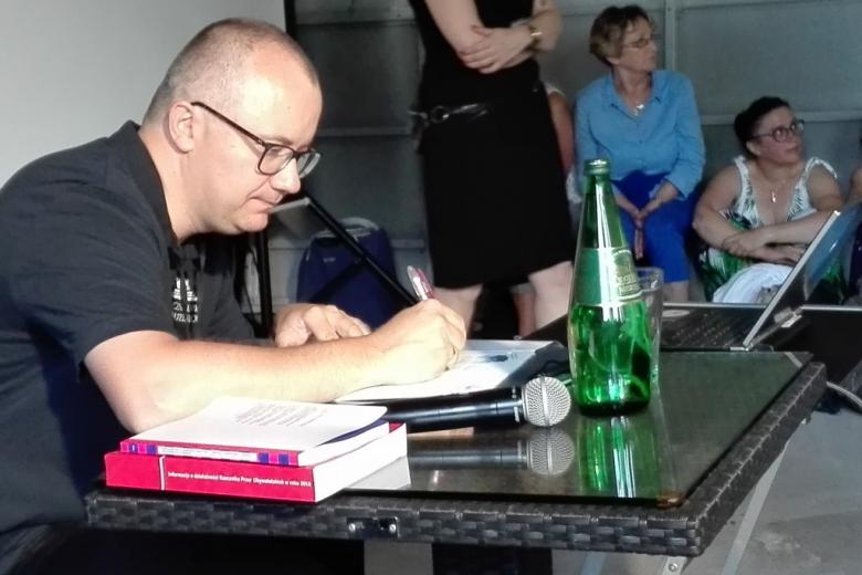 Mężczyzna podpisuje książkę, obok leży informacja roczna RPO